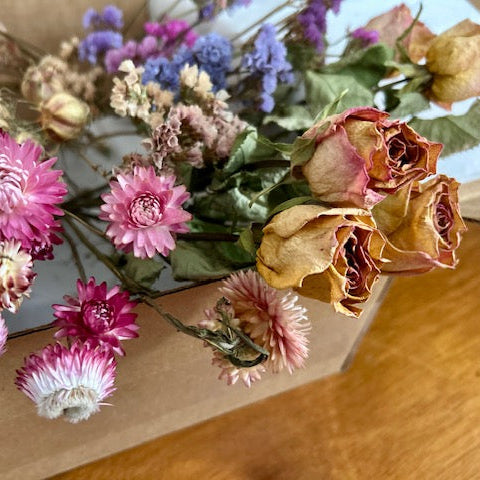 Dried flowers in a cardboard box on a wooden surface with a blurred background