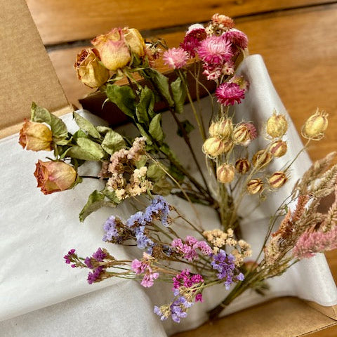 Dried flowers on white tissue paper in a cardboard box with a wooden background