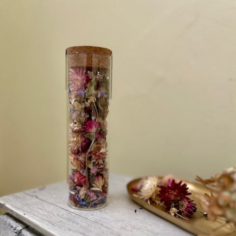 Clear cylindrical container with dried flowers on a wooden surface