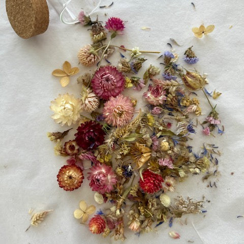 Dried flowers on a marble surface with a glass container and cork lid.