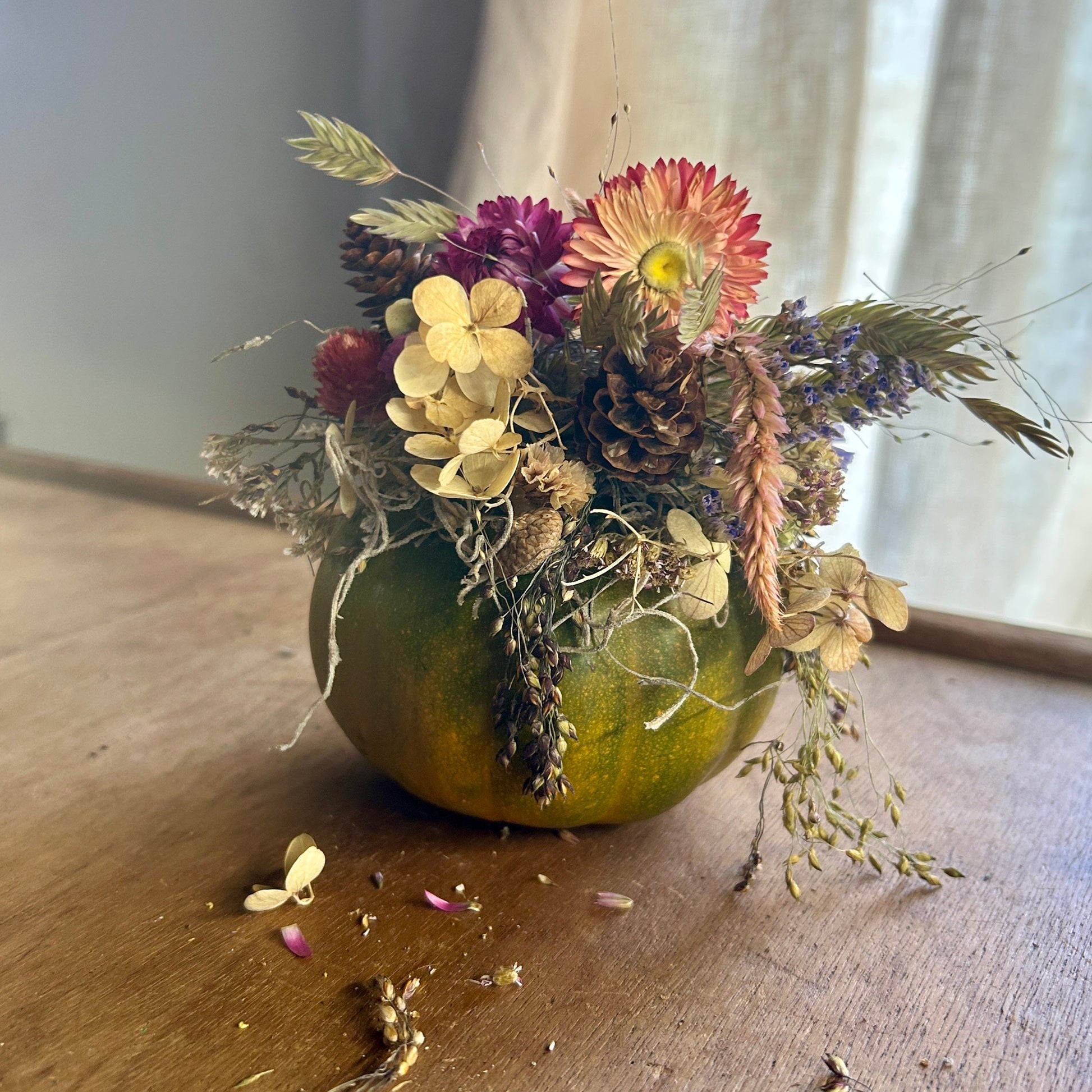 Decorative arrangement of flowers and leaves on a small green pumpkin on a wooden surface.